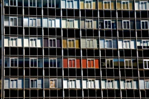 A close-up view of a multi-story apartment building with rows of windows and balconies, each displaying a variety of curtains, shutters, and reflections
